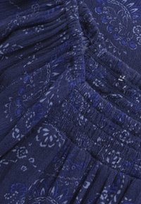 Marinefarbener Stoff mit einem floralen Paisleymuster und weißen Akzenten. Geschoppte Textur und Falten sorgen für räumliche Details. Weiches, leichtes Material.
