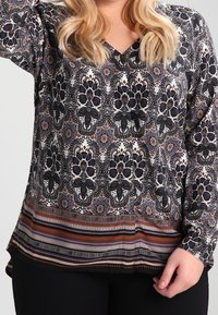 Langarmbluse mit floralem Muster in Schwarz, Weiß und Rost, mit gestreiftem Saum und V-Ausschnitt. Leichtes, strukturiertes Material.