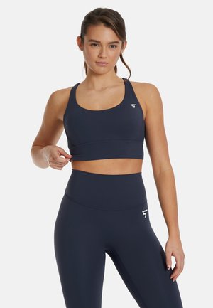 Reggiseno sportivo blu navy e leggings a vita alta, entrambi realizzati in tessuto liscio e elastico. Presentano un accento del logo sul lato sinistro del reggiseno e dei pantaloni.