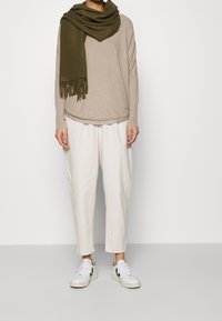 Beige tröja med lös passform och rund halsringning, tillsammans med vita vida byxor och vita sneakers med svarta detaljer. En olivgrön scarf hänger.