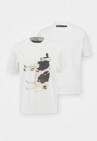 T-shirt de algodão branco com uma grande imagem impressa de uma vaca em preto e branco na frente. Colarinho redondo simples e mangas curtas.