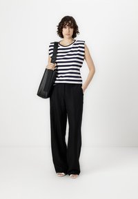 Striped sleeveless top in navy and white cotton, paired with loose black trousers. Accessories include a black shoulder bag with a long strap.