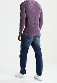 Pull en maille texturée violet associé à un jean denim bleu. Baskets blanches. Le pull est cintré ; le jean est à coupe décontractée avec des poches arrière.
