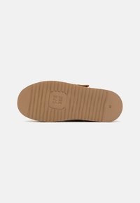Brown rubber shoe sole with horizontal ridges and embossed branding. Features a rounded shape and textured grip for traction.