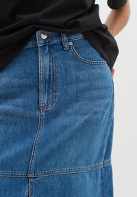 Denimkjol i medelblå med subtila blekningar, rakt snitt och synlig sömnad. Har knappstängning och sidofickor.