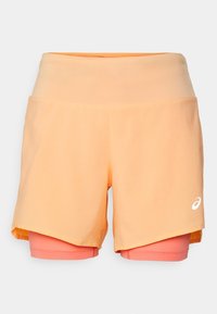 Persikkaväriset urheilushortsit, joissa on joustava vyötärö, kerroksellinen muotoilu ja valkoinen logo; sisältää vaaleanpunaisen sisävuorin lisätuen vuoksi.