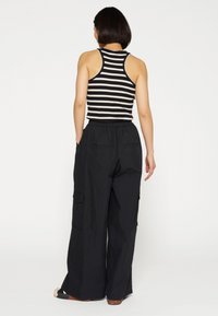 Zwarte high-waisted cargobroek met een relaxte pasvorm, twee zijzakken en een gestreept mouwloos top met zwarte en crèmekleurige horizontale strepen.