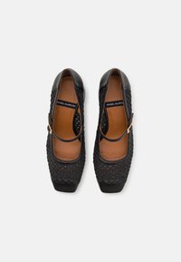Black leather Mary Jane shoes with a textured woven upper, square toe, and ankle strap. Features a brown insole and black accents.