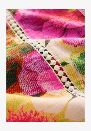 Livlig blomstret tekstil med lyserøde og gule nuancer, struktureret stof med hvid dekorativ kant langs sømmen.