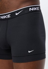 Κοντινή λήψη ενός ατόμου που φοράει μαύρα μποξέρ της Nike με λευκό λογότυπο στη ζώνη μέσης και στο κάτω μέρος του ποδιού.