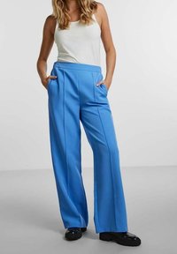 Blå vida byxor i en slät tygkvalitet, med hög midja, två framfickor och pressade veck för extra detaljer.