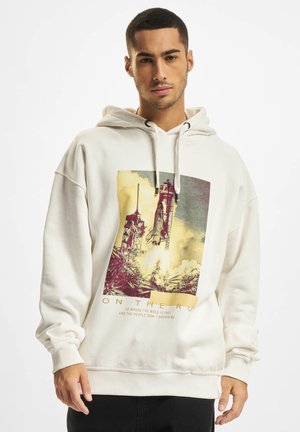 Creme hoodie i bomuldsblanding med grafisk print af en raket og tekst i midten. Den har en hætte med snørebånd og ribbede manchetter.