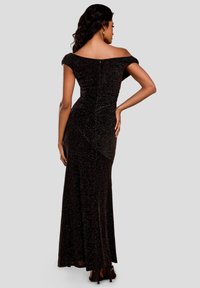 Donna con lunghi capelli scuri vestita con un abito da sera nero glitterato scollato e tacchi neri, posata con una mano sui fianchi.