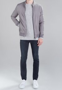 Lichtgrijze bomberjack, geribbelde grijze trui, donkere jeans en witte sneakers. Soepele stof en minimalistisch ontwerp zonder zichtbare logo's.