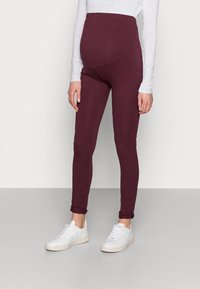Maternity leggings in burgundy, made of stretchy material, featuring a high waistband for support and fitted ankles, paired with white sneakers.