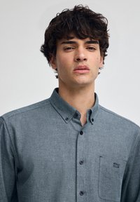 Knappad skjorta i mörkblått tyg med texturerad yta, med en bröstficka och broderad "POLO CLUB"-logotyp, samt svarta knappar.