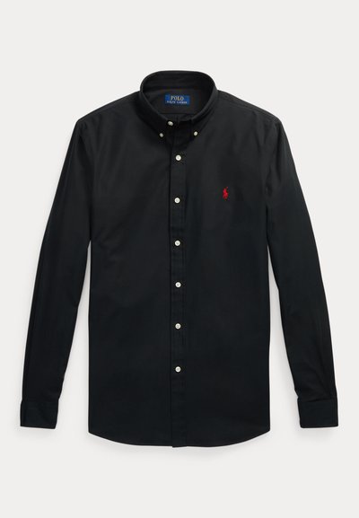 Zwarte blouse met lange mouwen en knopen, met rood logo op de linkerborst en een knoopsluiting aan de kraag, plat gelegd op een lichte achtergrond.