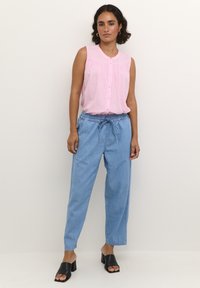 Rosa ärmlös blus med knapppdetaljer, i kombination med ljusblå, löst sittande byxor med elastisk midja och dragsko. Svarta sandaler som glider på.