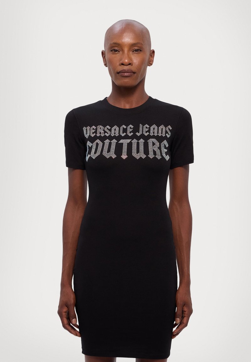 Čierne priliehavé šaty s krátkymi rukávmi, s logom "Versace Jeans Couture" v metalicky striebornom písme cez prsia. Hladká textúra.