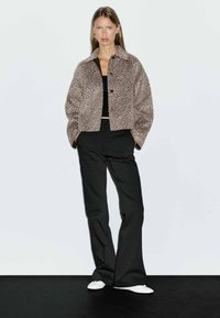 Giacca corta con stampa leopardata realizzata in tessuto testurizzato, abbinata a pantaloni neri a vita alta e scarpe slip-on bianche.