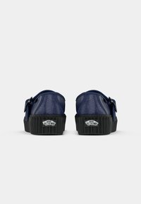 Een paar marineblauwe Vans sneakers met zwarte ribbelzolen, gezien vanaf de achterzijde met de "Vans Off The Wall" logo's op de hielen.