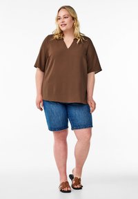 Haut beige à col en V avec des manches courtes, associé à un short bermuda en denim bleu. Les sandales présentent un design brun avec des accents décoratifs.