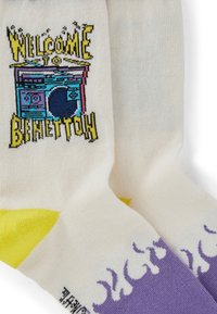 Witte sokken met gele hakken en paarse vlammen op de tenen, met pixelart-stijl tekst en een blauwe boombox met de tekst "Welcome to Benettow."