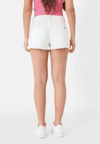 Shorts de mezclilla blanca con dobladillos deshilachados, de cintura alta y dos bolsillos traseros; combinados con zapatillas blancas y una camiseta de tirantes rosa.