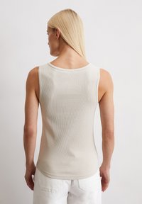 Lichtbeige mouwloze top met een geribbelde textuur, ronde halslijn en een getailleerde pasvorm, gecombineerd met witte high-waisted broek.