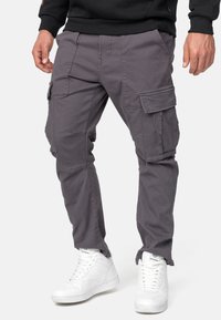 Pantalones cargo grises con múltiples bolsillos, ajuste entallado y tejido duradero. Combinados con zapatillas altas blancas para un contraste.