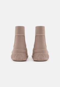 Zapatillas altas de goma rosa suave, con un acabado mate liso, detalles moldeados en los laterales y suelas texturizadas para mayor agarre.