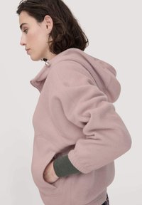 Felpa con cappuccio fucsia in pile, dotata di colletto con zip, cappuccio e tasche frontali. Presenta polsini a costine e una vestibilità rilassata per comfort e calore.