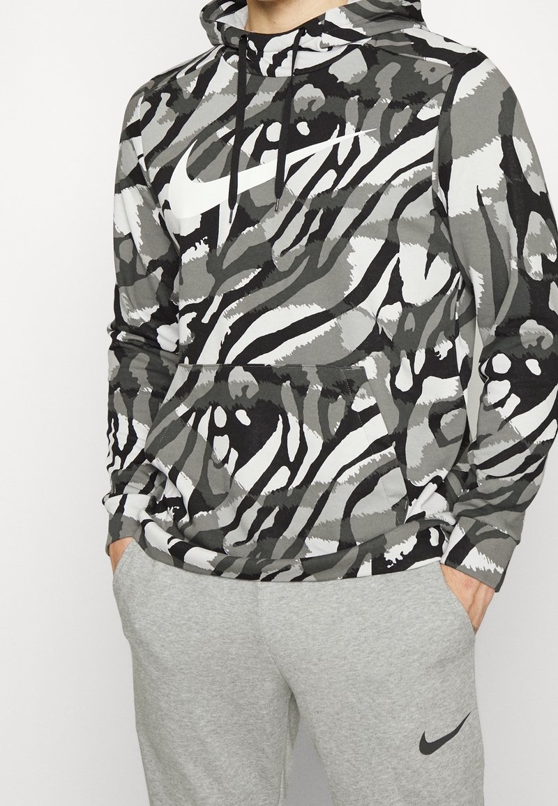 Homme portant un sweat à capuche Nike à motif zèbre noir, blanc et gris avec poche avant et un pantalon de survêtement Nike gris clair les mains dans les poches.