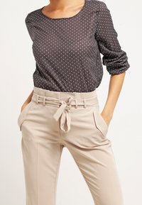 Blusa a pois grigio scuro con collo rotondo e maniche lunghe, abbinata a pantaloni beige chiaro con cintura e tasche laterali.