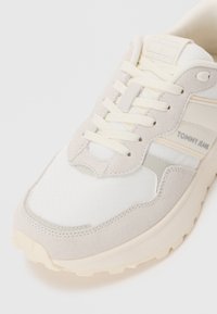 Baskets beige clair avec un mélange de matériaux lisses et texturés, bout rond, branding discret et accents blancs contrastants.