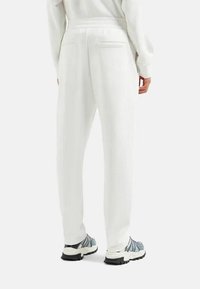 Pantaloni bianchi relaxed-fit con una texture liscia, due tasche posteriori e una cintura elastica. Abbinati a scarpe sportive grigie e blu.