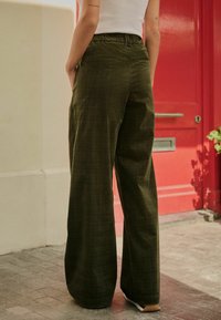 Pantaloni largi, de culoare verde măslin, confecționați dintr-un material texturat, având o talie înaltă și un model discret în carouri, cu două buzunare pe spate.