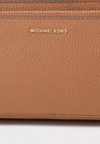 Hellbraune Leder-Geldbörse mit genarbter Oberfläche, goldfarbenen Beschlägen und geprägt eingraviertem Markennamen, die einen Reißverschluss an der Oberseite sowie eine glatte Oberfläche aufweist.