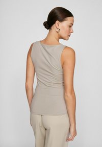 Beige sleeveless top with a round neckline, featuring gathered texture along the back, paired with matching beige pants.