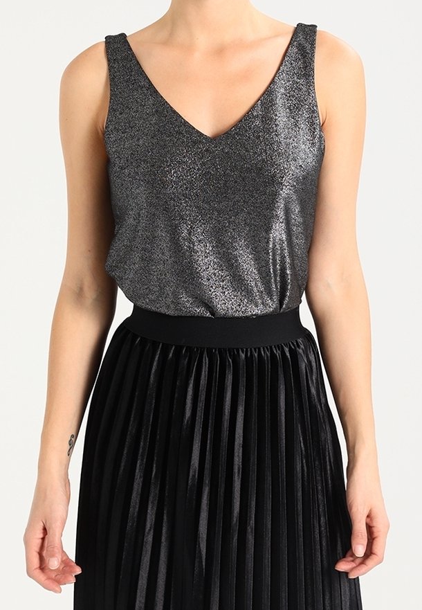 Silber schimmerndes Tanktop mit V-Ausschnitt, kombiniert mit einem hoch taillierten schwarzen Faltenrock. Der Rock hat eine strukturierte, glänzende Oberfläche.