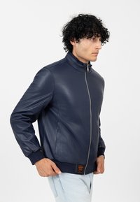 Veste en cuir marine avec un col haut, fermeture éclair, poignets côtelés et un accent texturé près de l'ourlet. Fini lisse, design ajusté.