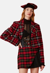 Rood en zwart plaid blazer met gestructureerde schouders, gecombineerd met een doorschijnend zwart top en een geplooide plaid rok met een gesp-accent.