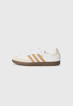 Biały skórzany sneaker z beżowymi paskami, beżowymi akcentami na palcach i pięcie, brązową fakturowaną podeszwą oraz napisem „SAMBA” z boku.