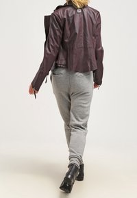 Burgundy läderjacka i cropped-modell med krage, i kombination med ljusgrå sweatpants. Ankelstövlar fulländar outfiten och betonar en avslappnad stil.
