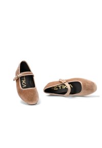 Zapatos Mary Jane en suave terciopelo beige con punta redondeada, detalle de hebilla lateral y una plantilla negra con branding dorado.