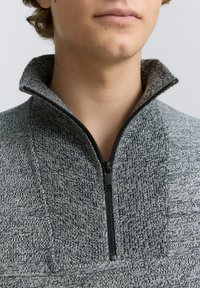 Pulover din fleece gri cu fermoar, cu guler înalt, design tricotat texturat și accente contrastante din negru la fermoar.