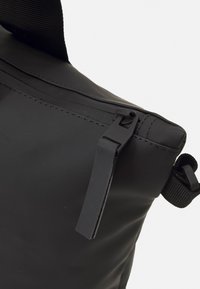 Borsa nera impermeabile con una superficie liscia, chiusura con zip e una tracolla intrecciata per il trasporto. Design minimalista con una silhouette elegante.