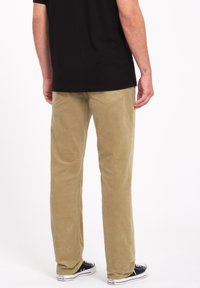 Pantalones de pana color beige claro con un ajuste slim, que cuentan con bolsillos traseros y se combinan con zapatillas negras. La tela tiene una textura acanalada.