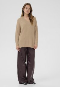 Beige ribbad stickad tröja med V-ringning, kombinerad med vida maroonfärgade byxor i konstläder och svarta skor med vita detaljer.