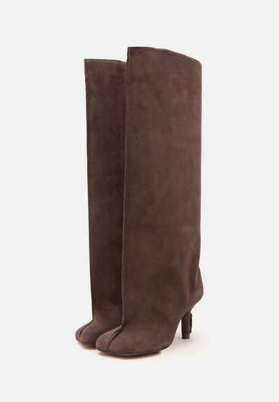 Paire de bottes hautes en daim marron avec un design à bout fendu et des talons hauts et fins sur un fond uni.